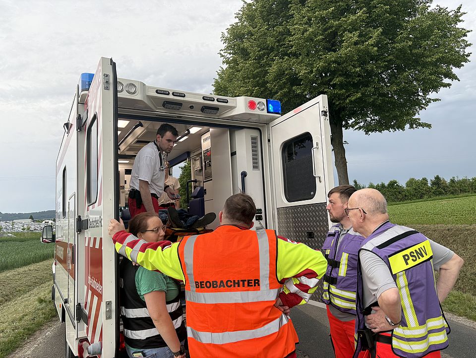 Rettungsdienstübung Uslar: DRK-Rettungswagen mit Auszubildendem, davor stehen Beobachter, Praxisanleiter und Mitarbeitende der PSNV und schauen in den Wagen