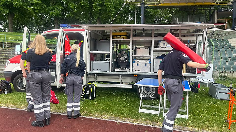 DRK-Bereitschaft beim Sanitätsdienst beim Frühjahrsvolkslauf in Göttingen im Jahnstadion: Bereitschaftsmitglieder in Uniform bauen stehen vor einem Wagen mit verschiedenen Materialien