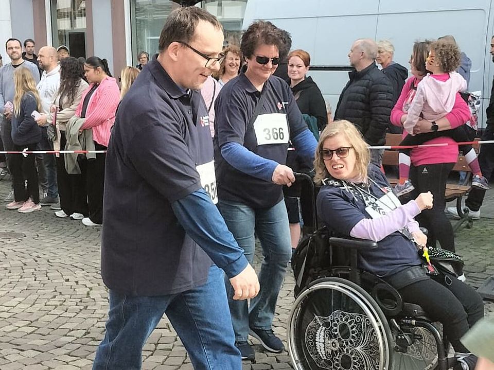 Mitglieder des FED des DRK laufen beim Bierstadtlauf in Einbeck mit, im Hintergrund Fachwerkhäuser und eine Person im Rollstuhl