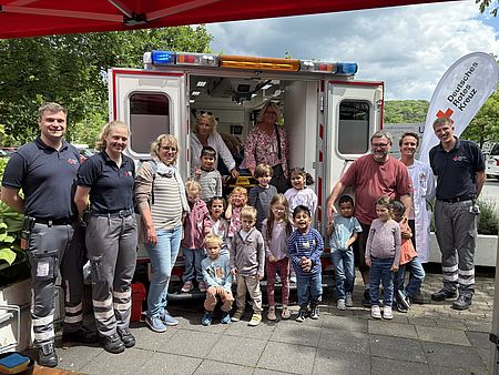 Kinder aus der DRK-Kita Bovenden und Ehrenamtliche stehen vor einem geöffneten Rettungswagen mit DRK-Logo. Die Gruppe ist auf dem Gelände der UMG Göttingen versammelt.