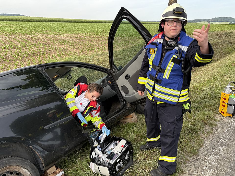 DRK-Rettungsdienstübung Uslar: Eine Auszubildende in rot-gelber Uniform lehnt sich auf der Autotür, um etwas auf der Medizintasche zu holen, im Vordergrund Einsatzleiter der Feuerwehr