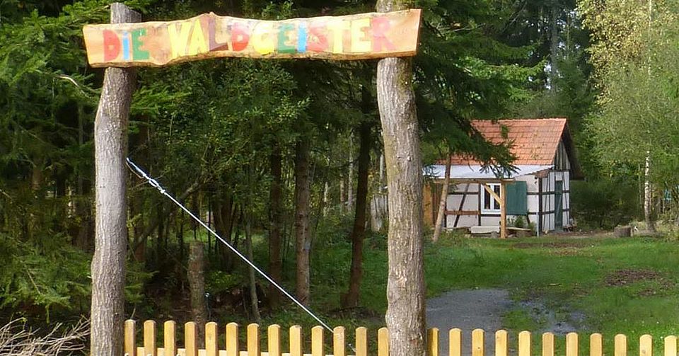 Holztor bunt bemalt als Eingang zum Kitagelände mit kleinem Häuschen im Hintergrund