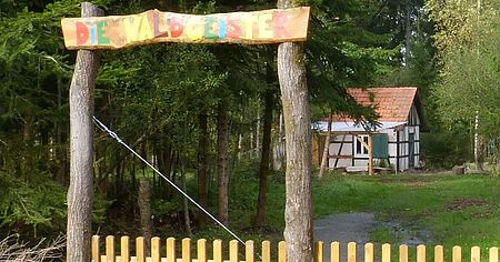 Holztor bunt bemalt als Eingang zum Kitagelände mit kleinem Häuschen im Hintergrund