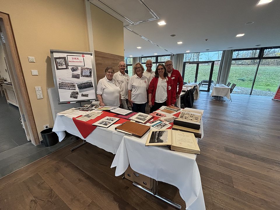 Kreisversammlung Gruppenfoto MA Personenauskunftsstelle Ehrenamtliche Mitarbeiterinnen stehen hinter einem Tisch mit historischen Dingen des DRK, die Teil eines Historien-Parcours sind
