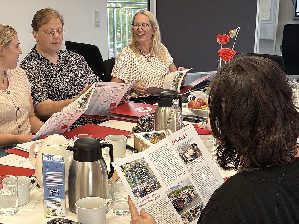 2026_10_01_Teamtag_Kita_Löwenhagen__10_.jpg Die Teilnehmenden sitzen gemeinsam an einem Besprechungstisch und beschäftigen sich mit Strukturen, Werten und Arbeitsweisen des DRK. Blättern in der Broschüre des DRK-Kreisverbandes Göttingen-Northeim.