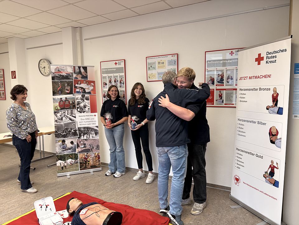 2026_08_18_FSJ_EH_Verabschiedung_Lars_Begrüßung_Finia__Lena_Sophie_21_.jpeg Verabschiedung und Begrüßung im DRK-Kreisverband Göttingen-Northeim e. V.: DRK-Kreisgeschäftsführerin und Erste-Hilfe Bereichsleiter zusammen mit den alten und neuen FSJlern in Bereich Erste-Hilfe, Umarmung zur Verabschiedung, im Vordergrund eine Übungspuppe