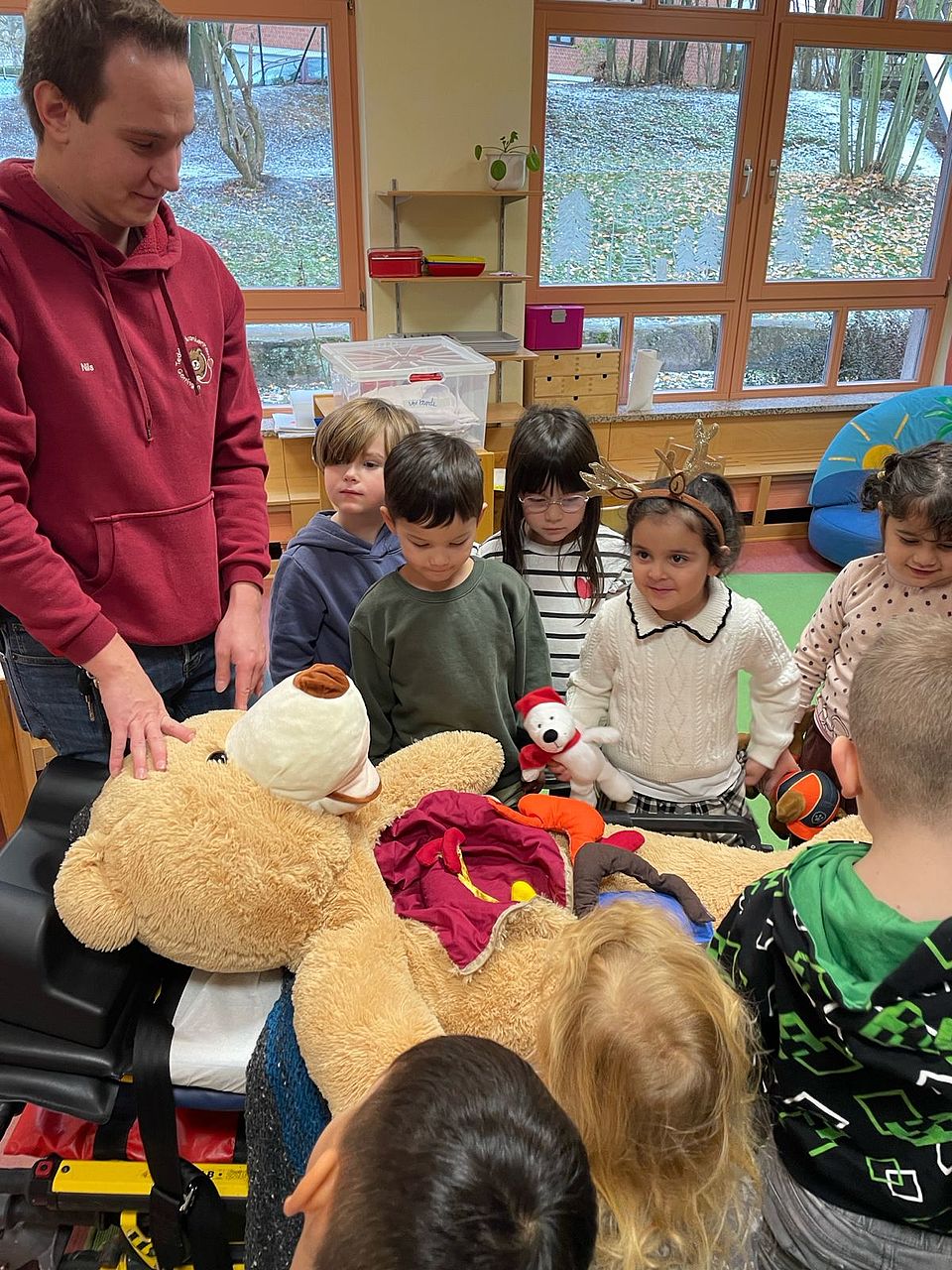 2025_11_24_Teddybärkrankenhaus__4 Ein Teddybär liegt in der Mitte und man sieht seine Organe, Kinder stehen drum herum, sowie auch der Leiter der Kita Bovenden, Matthias Henne