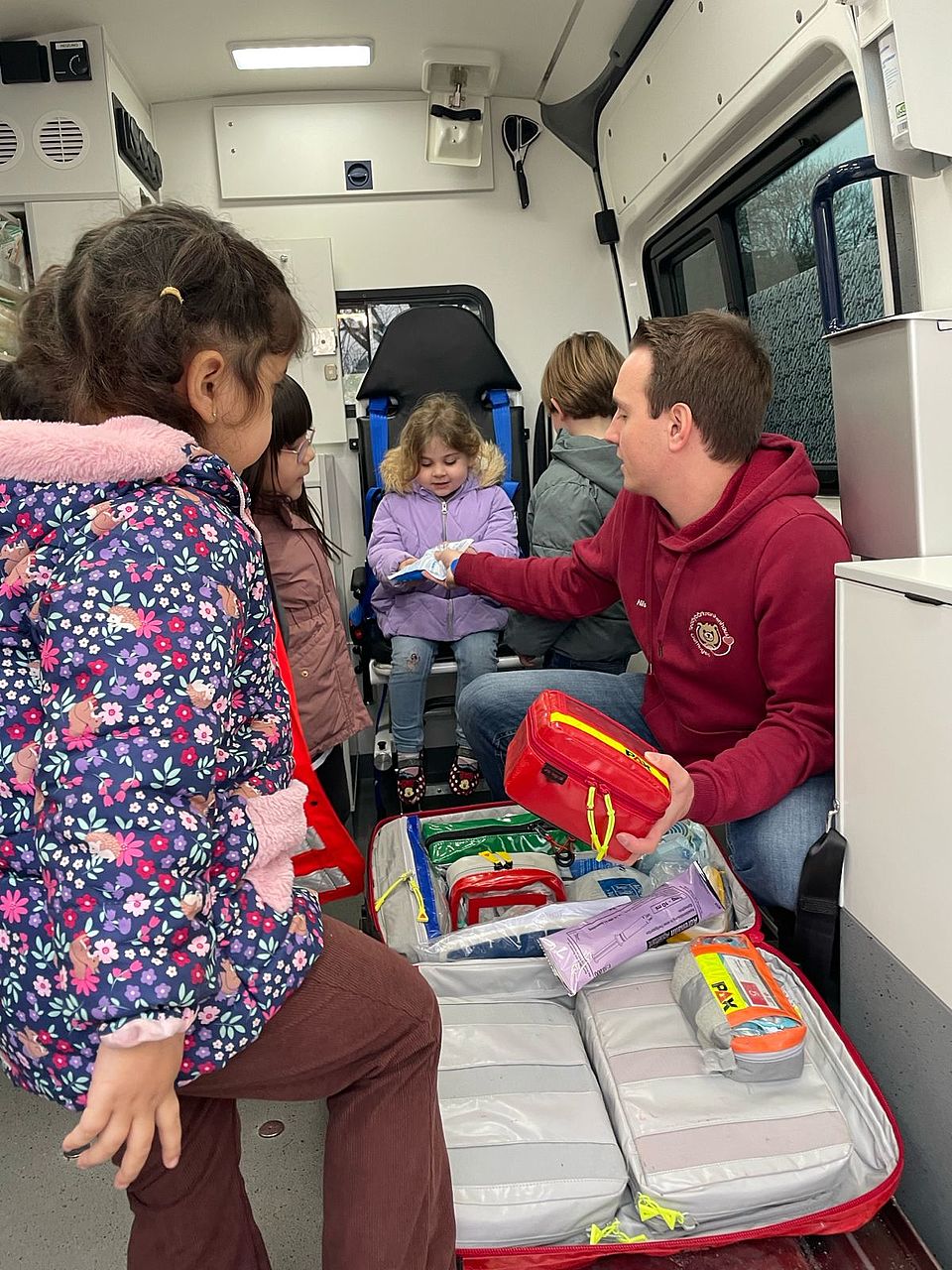 2025_11_24_Teddybärkrankenhaus__2 Leiter der Kita Bovenden, Matthias Henne, ist mit mehreren Kindern aus der Kita in einem Krankenwagen und alle schauen sich den Inhalt eines Verbandskoffers an