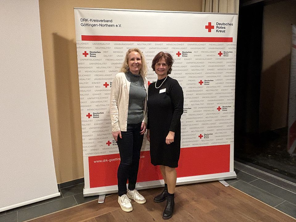 Kreisversammlung Frau Margraf und Frau Reußner Frau Margraf (Landtagsabgeordnete Gö) und Frau Reußner (Vorstandsvorsitzende des DRK-Kreisverbandes) stehen vor der DRK-Pressewand