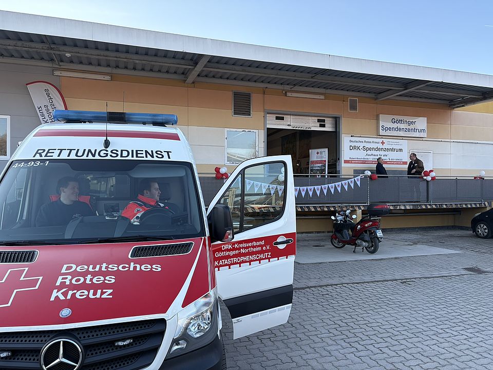 Ein DRK‑Rettungswagen steht mit geöffneter Tür vor dem Eingang des DRK‑Spendenzentrums Göttingen, das mit roten und weißen Luftballons und einer Wimpelkette für die Einweihung am 3. März dekoriert ist. Vor dem Gebäude befinden sich Gäste und Einsatzkräfte des DRK.