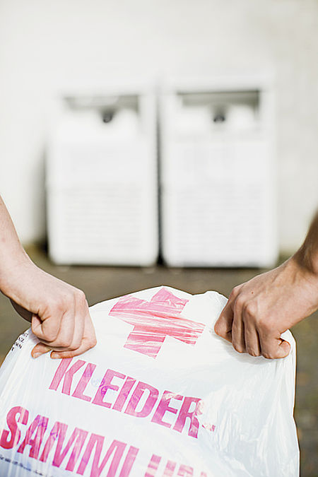 Zwei Hände halten eine weiße DRK-Sammeltüte für Altkleider 