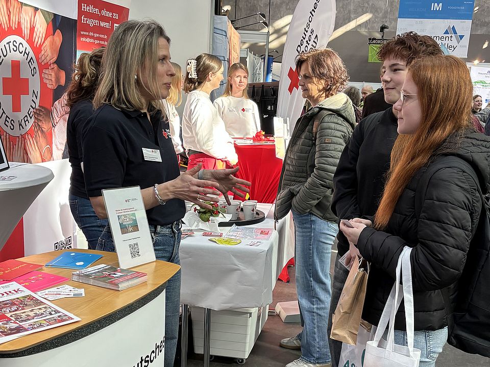 Stehtisch des DRK‑Kreisverbands Göttingen‑Northeim e. V. beim GöBit 2026. Eine DRK‑Mitarbeitende spricht mit einer Besucherin. Auf dem Tisch liegen Flyer, Becher und weitere Informationsmaterialien.