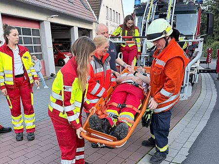 Übung „Rettung in Höhe und Tiefe“ in Uslar: DRK-Kreisverband Göttingen-Northeim e. V. und Feuerwehr transportieren Person auf Schleifkorbtrage vor Feuerwehrhaus