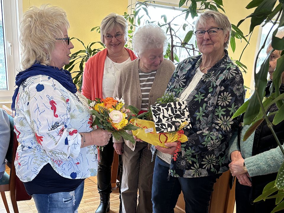 2026_03_JHV_2026-Neuer_Vorstand___Vorsitzende_Uslar__12_.jpeg Mitglieder des DRK-Ortsvereis Uslar stehen bei einer Geschenküberhabe mit Blumen bei einer Ehrung der und Verabschiedung der bisherigen Vorsitzenden Frau Andermann