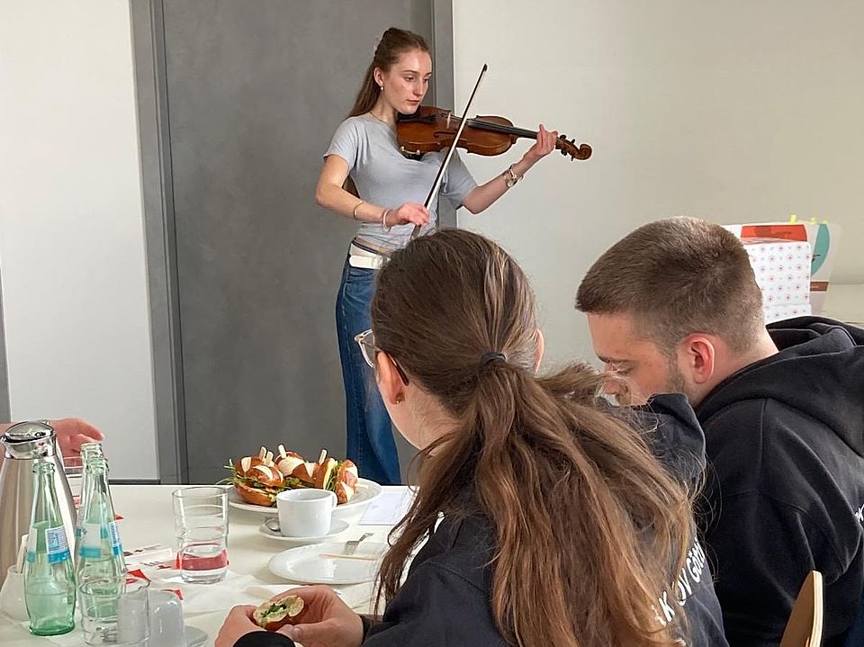 Geigerin Aenne Jeßing bei der Jahreshauptversammlung des DRK-OV Göttingen spielt Geige, im Vordergrund Mitglieder des Ortsvereins am Tisch