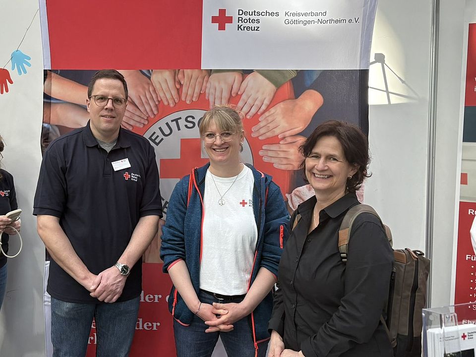 Messestand des DRK-Kreisverbands Göttingen-Northeim e.V. auf dem GöBit in der Lokhalle. DRK-Kreisgeschäftsführerin Petra Reußner und Mitarbeitende des DRK stehen vor einem Roll‑up mit DRK‑Logo