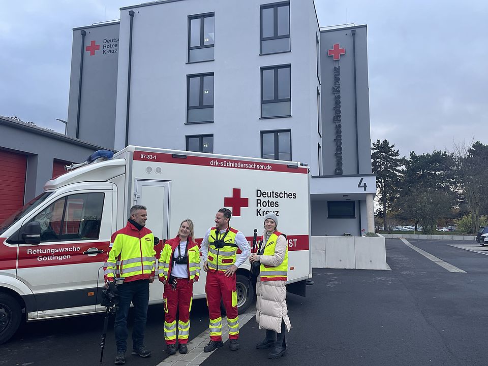 Man sieht die die beiden Zeitspuren.TV Redakteur*innen Sophie Kerkmann und Alexander Scheinert bei Ricarda Jung und Johannes Hartdegen von der DRK-Rettungswache vor einem Rettungswagen auf dem Hof des DRK-Kreisverbandes Göttingen-Northeim e. V.