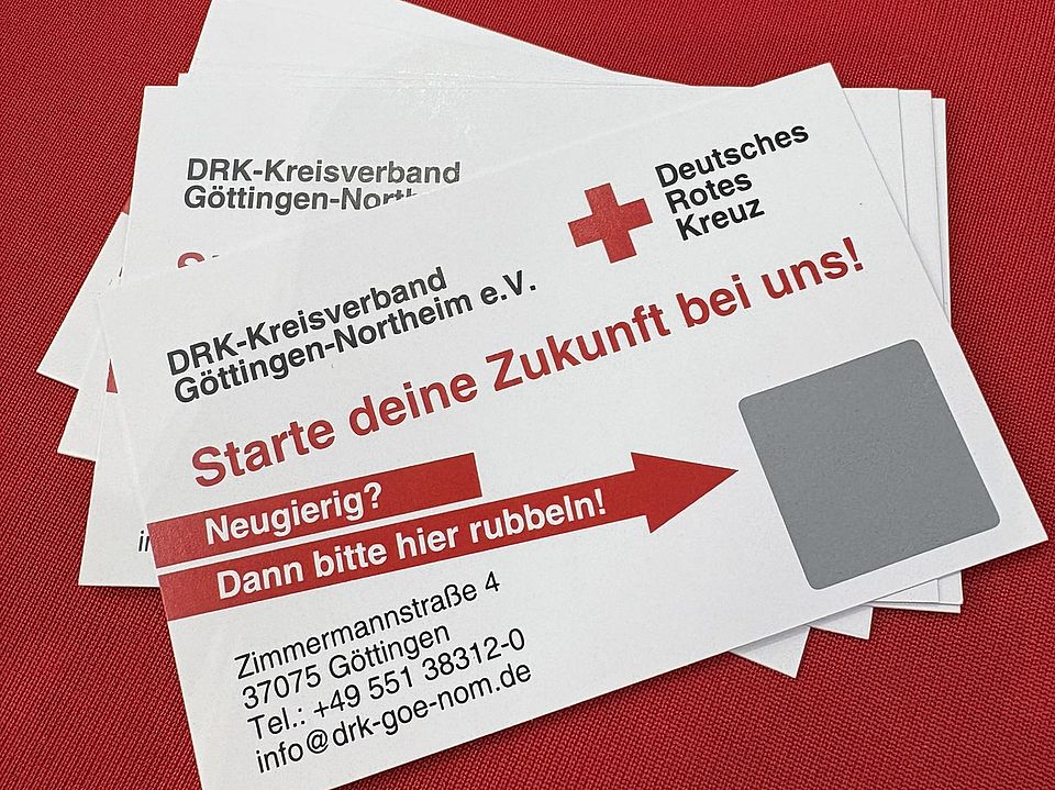 Nahaufnahme von DRK‑Rubbelkarten auf einem roten Tisch beim GöBit 2026 in der Lokhalle Göttingen. Die Karten tragen den Aufdruck ‚Starte deine Zukunft bei uns‘ sowie Kontaktangaben des DRK‑Kreisverbands Göttingen‑Northeim e. V.