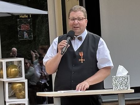 Jan Störmer mit Bundesverdienstkreuz spricht mit Mikrofon beim DRK-Kreisverband Göttingen-Northeim e. V. im Haus des Jugendrotkreuzes Einbeck