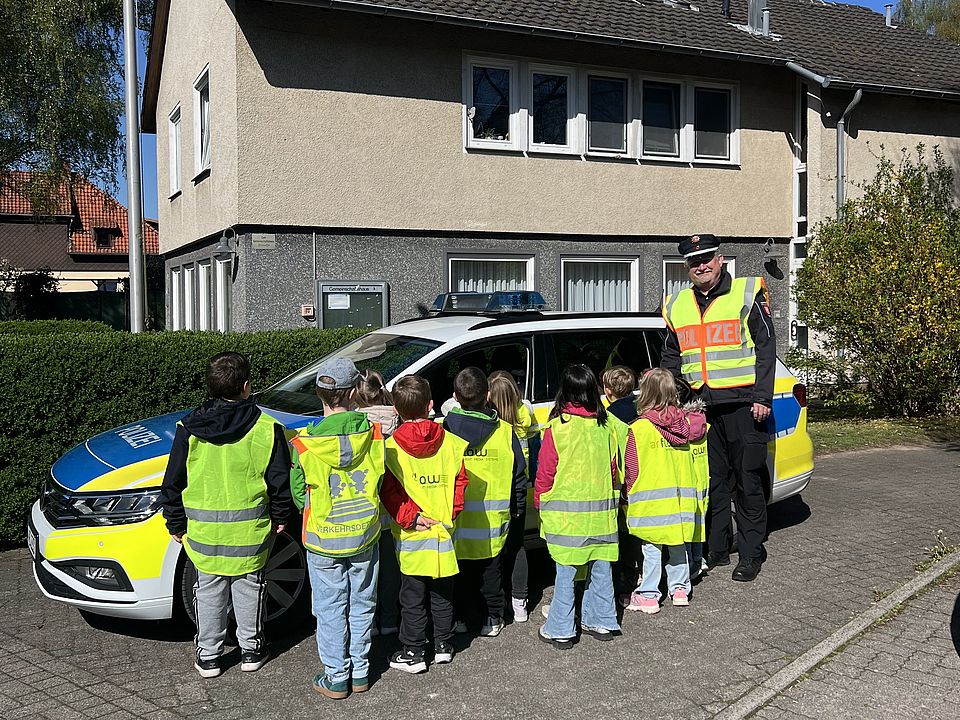 2026_04_27_Vorschularbeit_Kita_Volkmarshausen__2_.jpeg Kinder der DRK-Kita Volkmarshausen in gelben Warnwesten stehen vor einem Polizeiauto mit einem Beamten im Rahmen ihrer Fußverkehrsprüfung