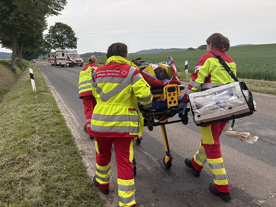 Rettungsdienstübung Uslar: drei Auszubildende des DRK-Rettungsdienstes in rot-gelber Uniform laufen mit Pateintenliege und Patientin und Tasche zum Rettungswagen