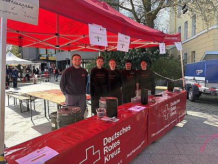 Helfer*innen und Mitglieder der DRK-Bereitschaft bei der Tour d'Energie 2026 in Göttingen beim Verpflegungsdienst vor einem Pavillion mit der Aufschrift 'Deutsches Rotes Kreuz' am Hiroshimaplatz