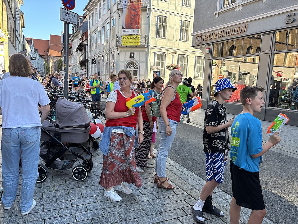 2026_07_01_Altstadt-Läuferinnen_während__1_.jpeg DRK‑Unterstützer*innen beim Altstadtlauf Göttingen 2026 mit Wasselpistolen am Streckenrand