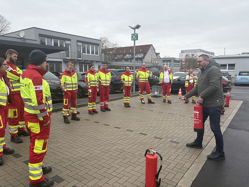 2026_04_13_Brandsschutzübung_im_Rettungsdienst__39_.jpg DRK-Rettungsdienst bei einer Brandschutzübung auf dem Hof des DRK-Kreisverbandes Göttingen-Northeim: Mitarbeitende des DRK-Rettungsdienstes stehen im Halbkreis und schauen einer Demonstration eines Feuerlöschers zu