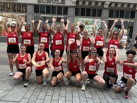 Mehrere Teilnehmende in roten DRK-Laufshirts stehen als Gruppe zusammen und heben die Arme. Das Team tritt gemeinsam beim Altstadtlauf in Göttingen an.