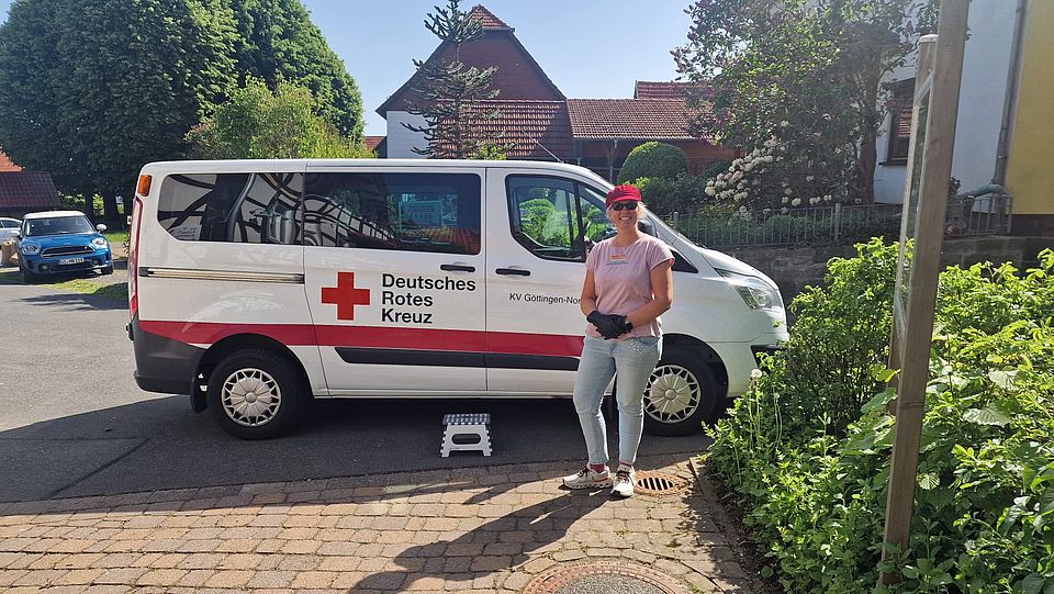 2026_05_26_Teamtag_Kita_Bühren__7_.jpeg Kita-Fachberaterin beim DRK, Jennifer Treichel, steht neben DRK-Fahrzeug mit Logo „Deutsches Rotes Kreuz – KV Göttingen-Northeim“ in Wohnstraße.