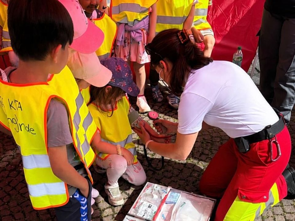 DRK-Einsatzkraft erklärt Kindern Erste Hilfe mit Verbandsmaterial beim Bienenmarkt Uslar.