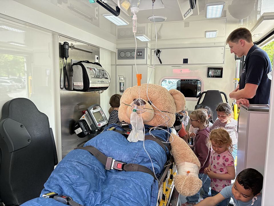 2026_06_01TBK_Teddybärkrankenhaus_UMG__Kita_Bovenden_1_.jpg Großer Teddybär auf Trage im DRK-Rettungswagen, Kinder untersuchen das Kuscheltier beim Teddybärkrankenhaus in der UMG Göttingen.