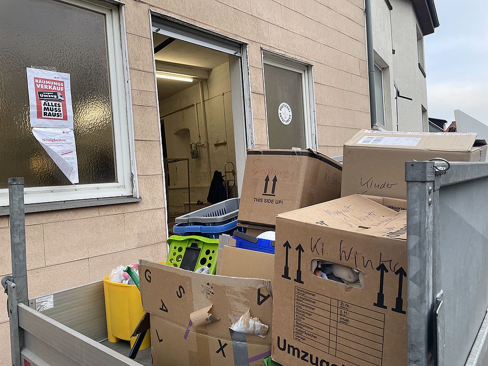 Ein Anhänger gefüllt mit Umzugskartons und Wäschewannen steht vor dem Gebäude, in dem sich der ehemalige DRK-Kleidershop befunden hat.