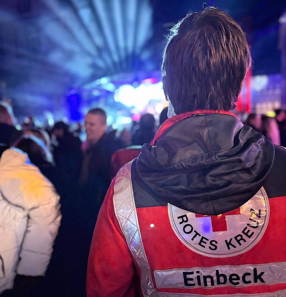 2026_10_10_Eulenfest_in_Einbeck_2026__11_.jpg Mitglied der DRK-Bereitschaft beim Eulenfest in Einbeck, im Hintergrund eine Bühne mit Beleuchtung und Menschen