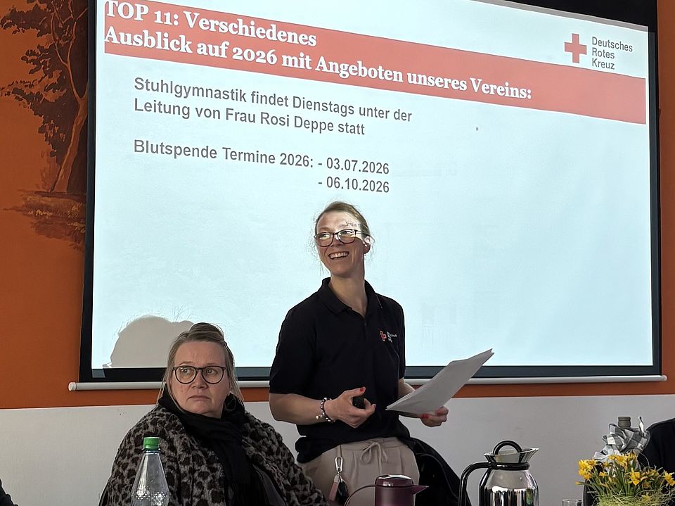 Präsentation zu Vereinsangeboten 2026 während der DRK-Jahreshauptversammlung Katlenburg mit Redebeitrag vor Leinwand.