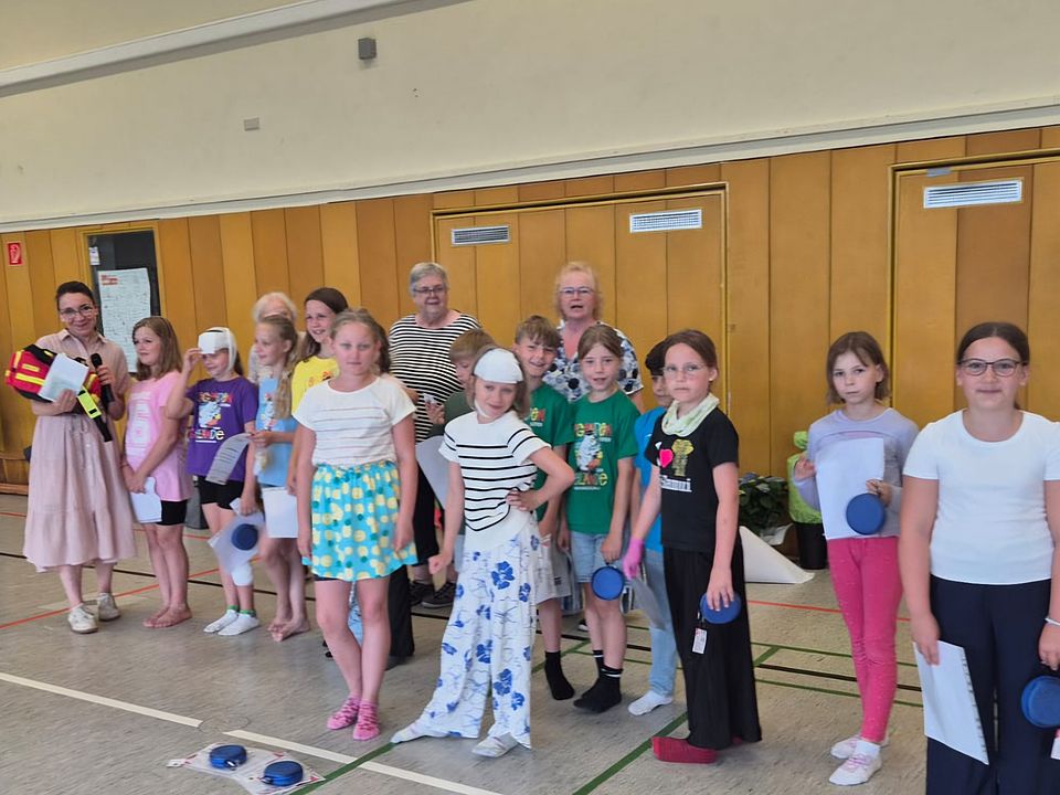 Gruppe von Schülerinnen und Schülern, die in einer Turnhalle stehen und von Ehrenamtlichen des Ortsvereins Urkunden für die Teilnahme überreicht bekommen