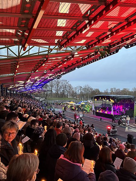 Man sieht die Ränge des Jahnstadions in Göttingen mit vielen Menschen, die zum Adventssingen dort sind. Im Hintergrund sieht man eine Bühne mit lila Beleuchtung