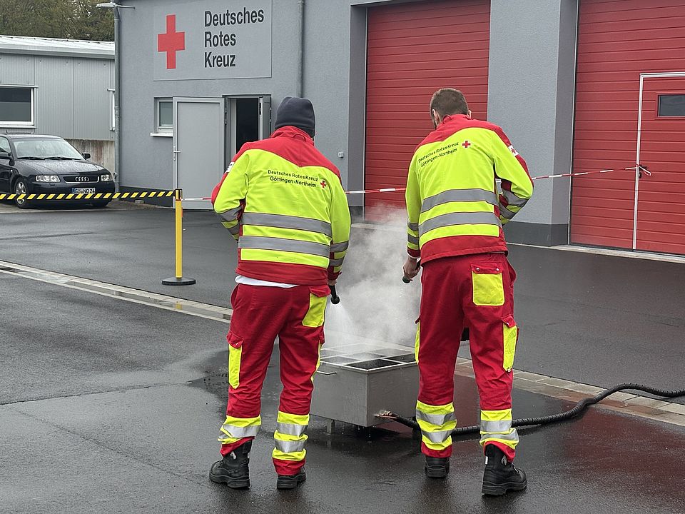 2026_04_13_Brandsschutzübung_im_Rettungsdienst__1_.jpg DRK-Rettungsdienst bei einer Brandschutzübung auf dem Hof des DRK-Kreisverbandes Göttingen-Northeim: Zwei Mitarbeitende des Rettungsdienstes in Uniform löschen ein Feuer auf dem Boden