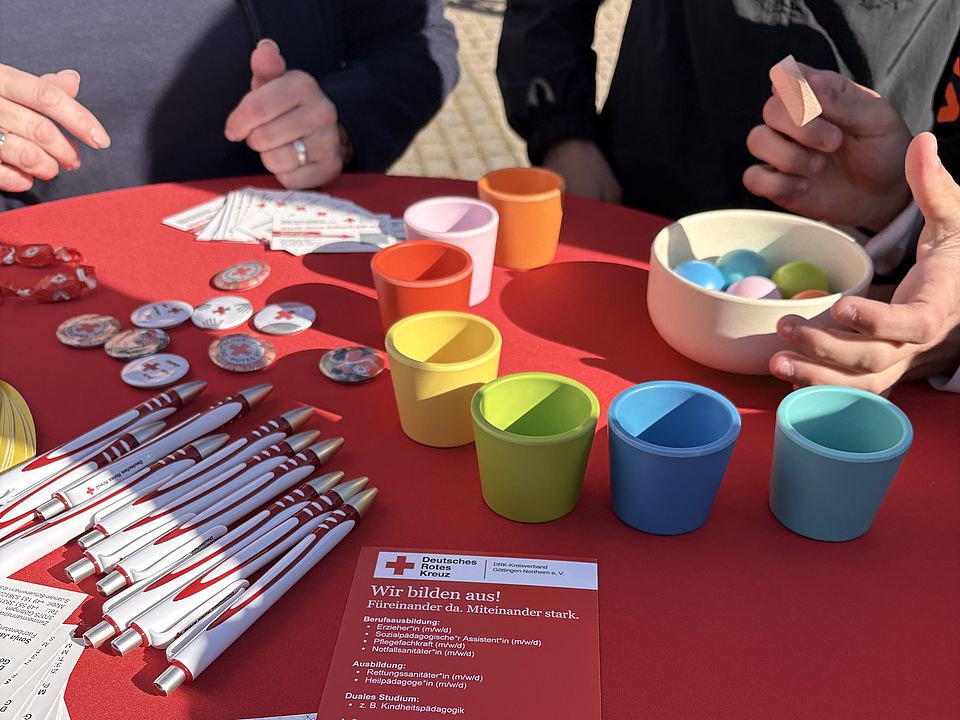 Schülerin der BBS Einbeck sortiert farbige Kugeln im Becher auf einem Stehtisch mit Infomaterialien, Mitmachaktion am DRK-Stand auf der Einbecker Ausbildungsmesse