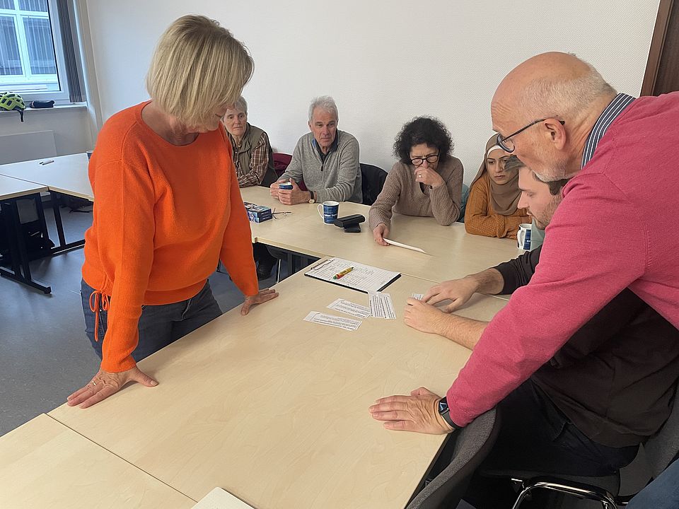 Die PASt Vorsitzende erläutert Teilnehmenden etwas am Tisch stehend