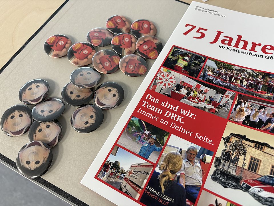 DRK‑Anstecker und eine Jubiläumsbroschüre des DRK‑Kreisverbandes Göttingen‑Northeim liegen bei der Familienführung der Evangelischen Familienbildungsstätte aus
