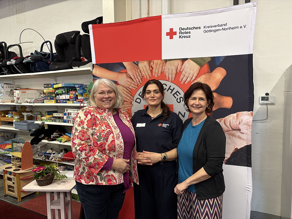2026_03_03_Spendenzentrum_Einweihung_Frau_Krause__Frau_Arif__Frau_Reußner.jpg Nawal Arif, Anja Krause, Petra Reußner stehen vor einem DRK‑Banner im Spendenzentrum Göttingen. Im Hintergrund sind Regale mit Second‑Hand‑Artikeln zu sehen, aufgenommen während der Einweihungsfeier am 3. März.
