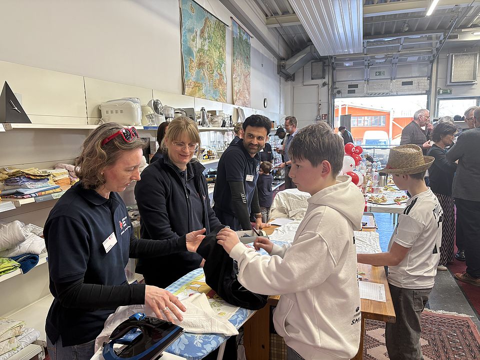 2026_03_03_Spendenzentrum_Einweihung_Atmosphere.jpg Engagierte Mitarbeitende und Ehrenamtliche des DRK unterstützen Kinder und Gäste an einem Aktionstisch im neuen Spendenzentrum Göttingen. Um sie herum stehen Regale mit Haushaltswaren und Spielen