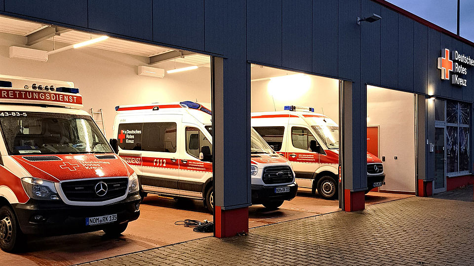 2026_01_29_Umzug_Bereitschaft_Einbeck__4_.jpg Man sieht die Rettungswache der DRK-Bereitschaft in Einbeck am Altendorfer Tor mit mehreren Einsatzfahrzeugen in einer offenen Garage bei Dämmerung