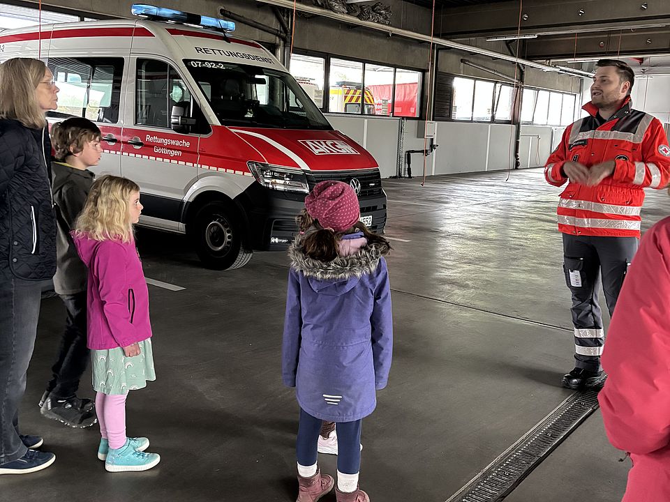 Besuchende der Evangelischen Familienbildungsstätte erkunden bei einer Familienführung den Fuhrpark des DRK‑Kreisverbandes Göttingen‑Northeim mit Rettungswagen und Einsatzfahrzeugen gemeinsam mit Mitgliedern der DRK-Bereitschaft