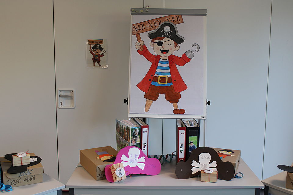 Ordner und gebastelte Geschenke mit Piraten-Motiv liegen auf einem Tisch vor einem Plakat mit einem gemalten Pirat und einem Ahoi Schild
