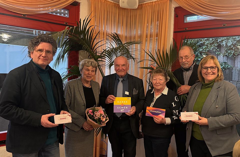 2026_02_12_1horiz_neuer_Teamvorstand___alter_VorstandIMG_0286__1_.jpg Eine Gruppe von sechs Personen steht in einem geschmückten Innenraum vor großen Pflanzen und einer hellen Fensterfront. Alle Personen stehen dicht nebeneinander und halten kleine Dankes‑ oder Glückwunschkarten in den Händen; eine Person hält zusätzlich einen Blumenstrauß. Die Personen tragen festliche oder gepflegte Alltagskleidung. Hinter der Gruppe hängen Vorhänge in warmen Farbtönen. Der Anlass des Fotos ist die Vorstellung des neuen Teamvorstands des DRK‑Ortsvereins Adelebsen. Im Rahmen der Veranstaltung wurden Dinah Stollwerck‑Bauer, Kerstin Paetsch (abwesend), und Dr. Thomas‑Carl Stiller als neuer Teamvorstand gewählt. Zudem wurden Hartmut Koch und Helga Koch für ihre langjährige Vorstandsarbeit gewürdigt. Auch Erika Hildebrandt und Horst‑Dieter Hildebrandt gehören zu den auf dem Bild gezeigten Personen. Die Bildszene zeigt die Gruppe während der offiziellen Übergabe und des Dankes an den bisherigen Vorstand.