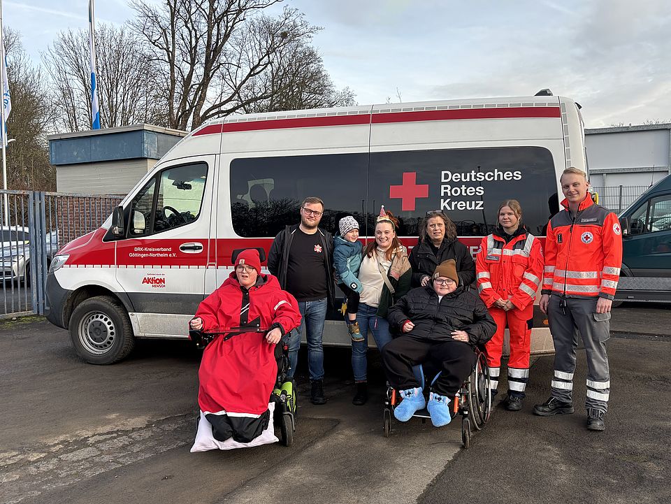 Ein Einsatzfahrzeug der Bereitschaft des DRK Göttingen-Northeim e. V. - davor stehen als Gruppenfoto Bereitschaftsmitglieder sowie Bewohner*innen des Hospizes Sternenlichter und Mitarbeitende des Hospizes. Zwei Personen sitzen im Rollstuhl