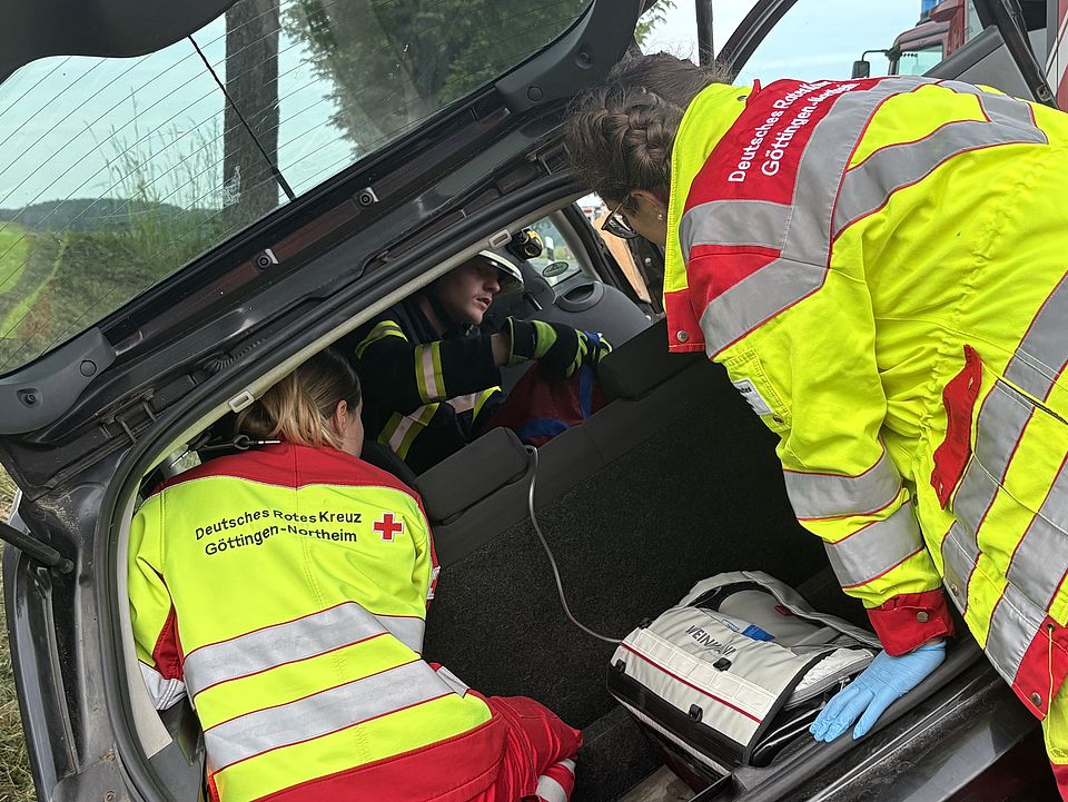 Rettungsdienstübung Uslar: drei Auszubildende des DRK-Rettungsdienstes in rot-gelber Uniform kümmern sich um Patientin vom Kofferraum des Autos aus