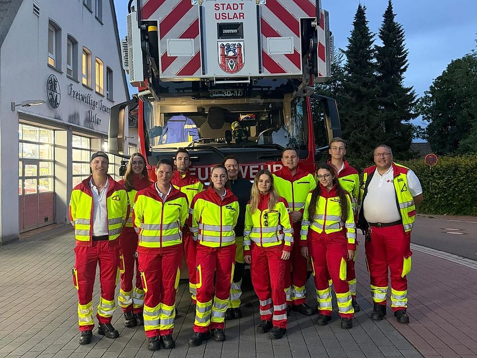 2026_06_03_Rettungsdienstübung_Uslar_mit_Feuerwehr_-_Rettung_in_Höhe_und_Tiefe__13_.jpeg Gruppenfoto nach Übung „Rettung in Höhe und Tiefe“ in Uslar: Einsatzkräfte von DRK-Kreisverband Göttingen-Northeim e. V. und Feuerwehr vor Drehleiterfahrzeug